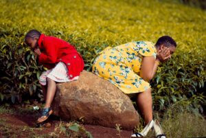 A woman and child seated back-to-back on a rock in a lush green field, deep in thought.